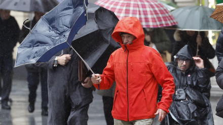 Un hombre trata de protegerse de la lluvia y el viento en Bilbao