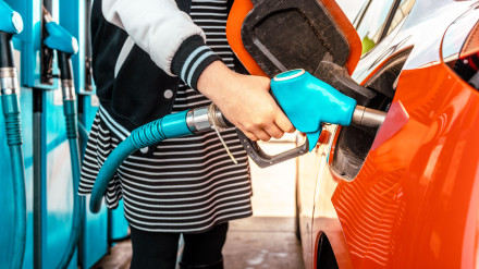 Mujer joven en una gasolinera, detalle de la mano repostando un coche