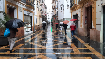 Gente con paraguas bajo la lluvia en la calle Corredera de Lorca