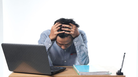 2DFXNBH a portrait of an Asian man with a tired expression working on computer reports and books. office employee with isolated white background