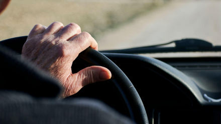 Manos de un jubilado sosteniendo el volante de un vehículo