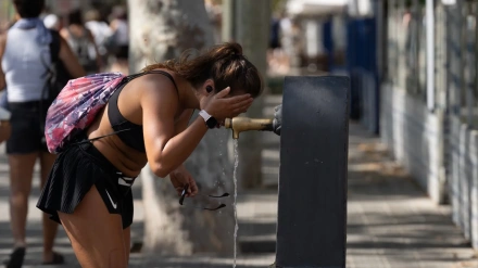 Una chica bebe agua de una fuente en Barcelona