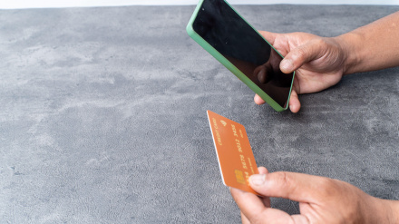 Manos sosteniendo una tarjeta de crédito genérica y un teléfono inteligente