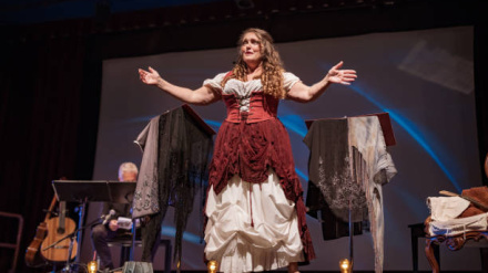 Mature woman Performer singing on the stage. She is dressed in period costume. Stage interior of Theatre during performance at night