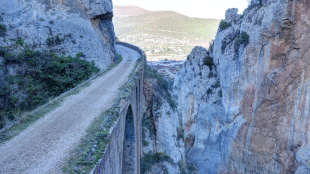 Un puente junto a un acantilado en Foz de Escalada, una brecha en las altas montañas rocosas del lago de La Pena, con árboles en las rocas, al atardecer, en Aragón, España.