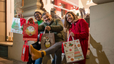 Happy friends showing Christmas shopping bags in front of a store at nigh
