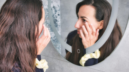 Mujer mirándose en el espejo del baño tocándose los ojos