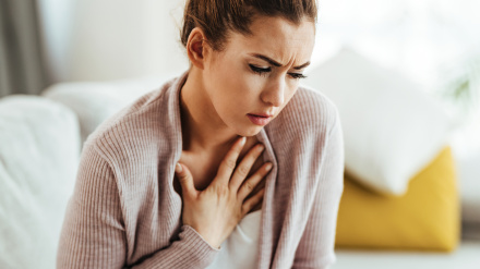 Young woman feeling sick and holding her chest in pain at home.