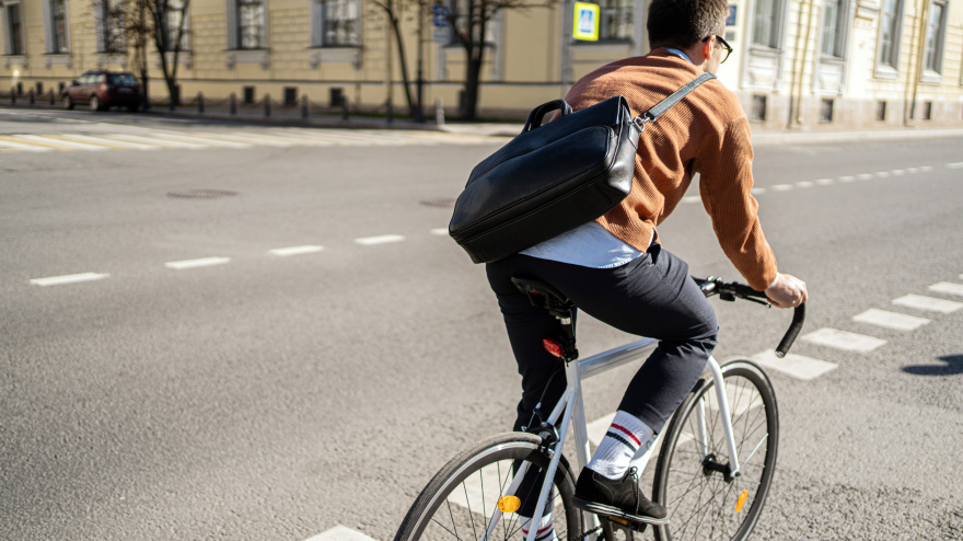 A cyclist with a briefcase rides a bicycle in the city to work.