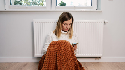 Mujer con una manta apoyada en la calefacción