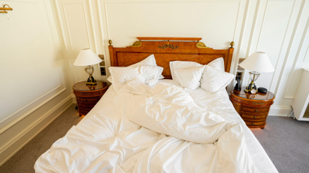 Cama sin hacer con sábanas arrugadas en una lujosa habitación de hotel vacía.