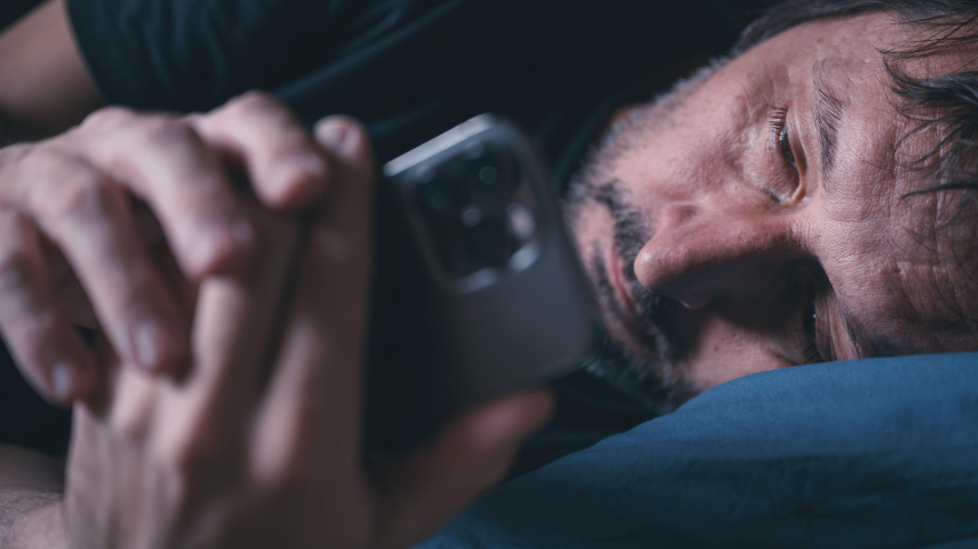Hombre usando un teléfono inteligente mientras está acostado en la cama tarde en la noche, concepto de insomnio, enfoque selectivo, concepto de FOMO