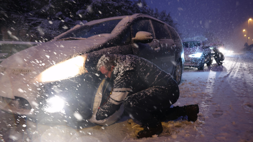 Un hombre coloca las fundas de nieve antideslizantes durante una nevada a primera hora en Torrelodones