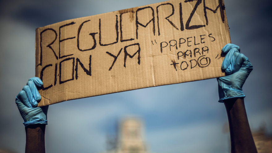 Una trabajadora doméstica migrante protesta por documentos y regulaciones sosteniendo una pancarta.