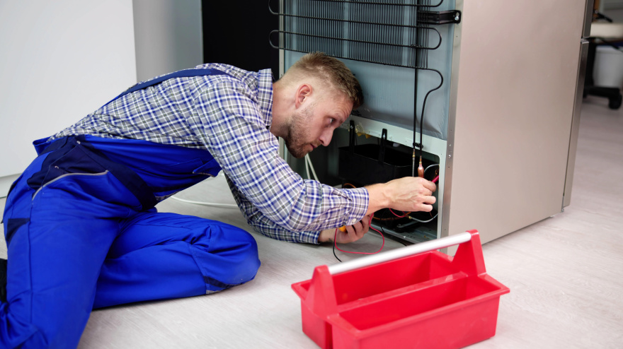 Un electricista hace una prueba de electrodomésticos con multímetro para reparar un refrigerador en casa