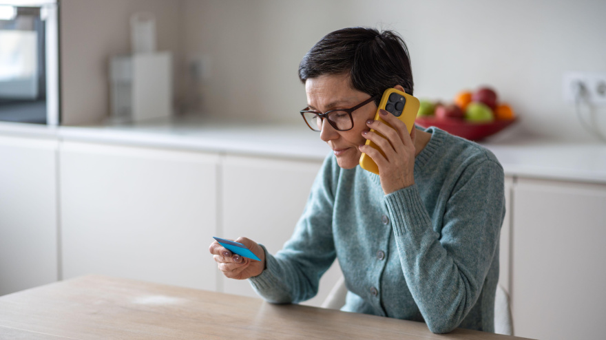 Una mujer madura, confundida y confiada, comparte los datos de su tarjeta de débito y crédito con un estafador desconocido que llama desde su casa.