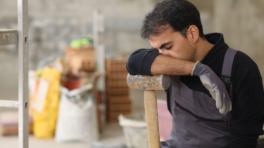 Trabajador de la construcción cansado descansando apoyado en un martillo en una casa en renovación