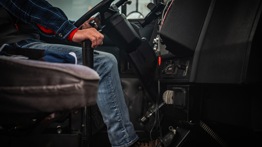 Una persona se sienta en un vehículo, con las manos en el volante, conduciendo activamente y concentrada en la carretera.