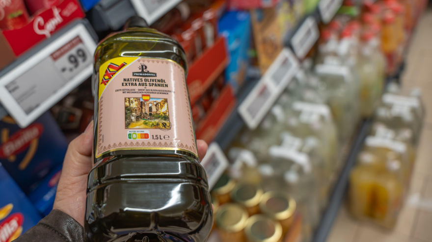 Mano sosteniendo una botella grande de aceite de oliva virgen extra en el pasillo de un supermercado