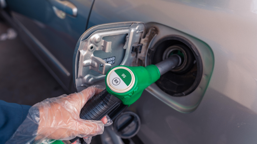 Pistolas de combustible en una gasolinera europea. Una mujer con un guante de plástico introduce una pistola verde de 95 E5 en el depósito.