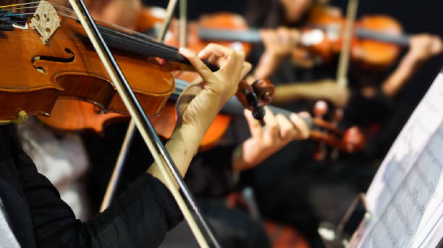 Hands playing violin orchestra with note sheet on stage