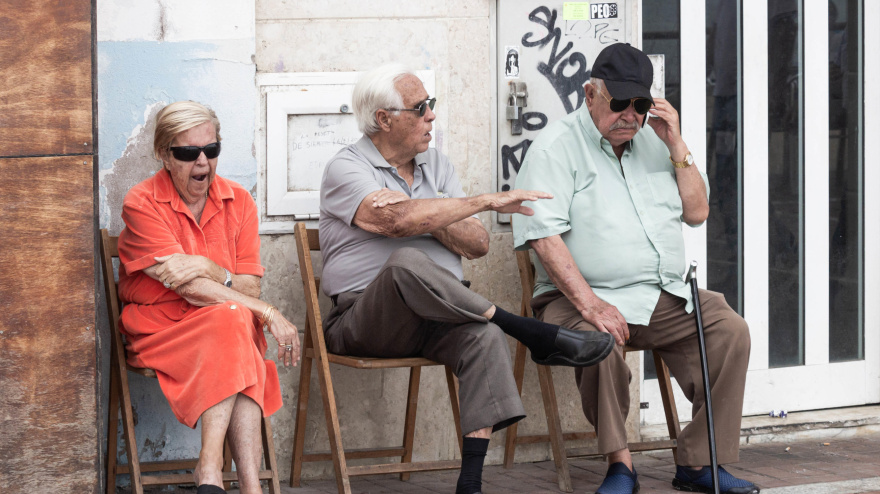 Dos hombres mayores y una mujer sentados en la calle en España