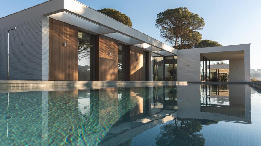 Modern white and wood luxury house with pool and pine trees outside.