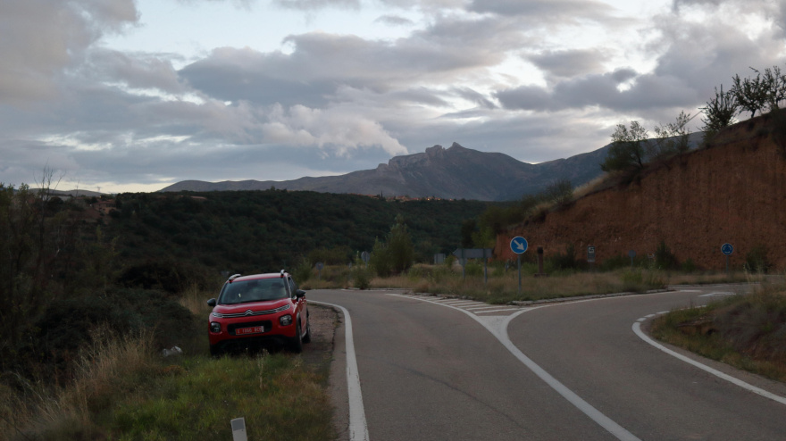 Paisaje de Aragón, España, con un atardecer nublado de otoño. Un coche rojo está aparcado junto a una rotonda (conducción por la izquierda) durante un viaje por carretera.