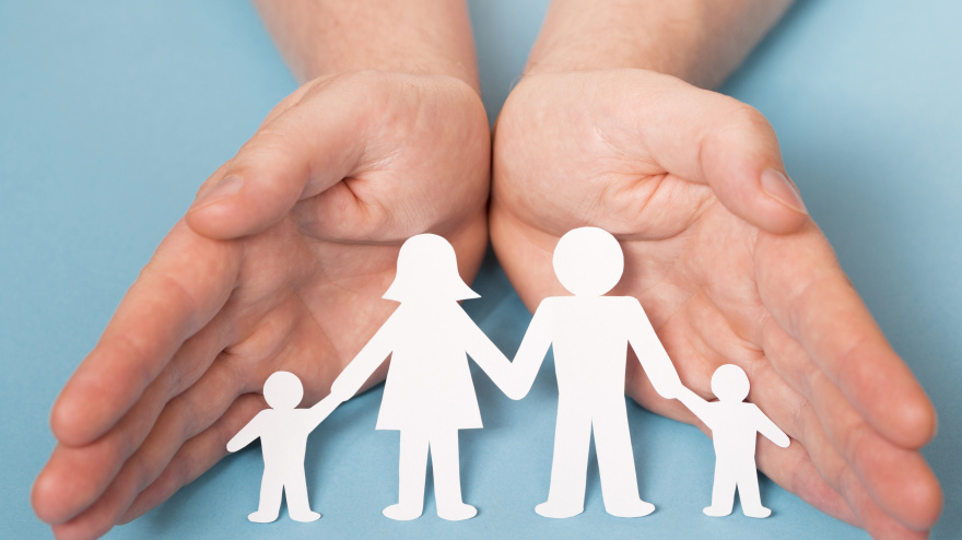 Dos manos protegen a siluetas de papel que representan familias e infancia