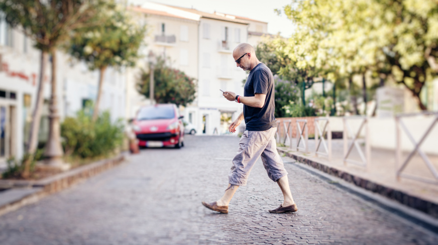 Un hombre cruza la carretera mirando su teléfono móvil