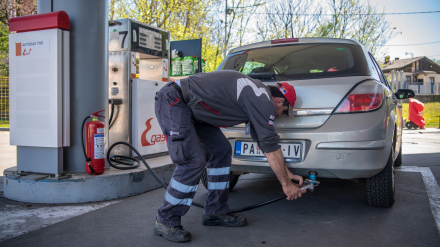 Repostaje de automóviles. Trabajador masculino en una gasolinera llenando un coche con combustible, repostando gas licuado de petróleo, GLP o GNT. Empleado sosteniendo un dispensador de GLP.