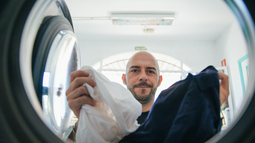 Un hombre carga la lavadora con ropa sucia en la lavadora.