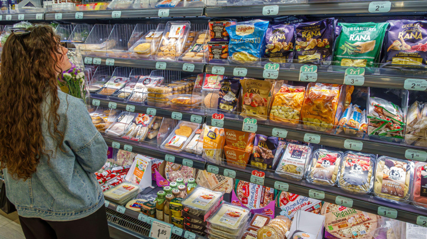 Una mujer frente a un estante del supermercado con comida preparada