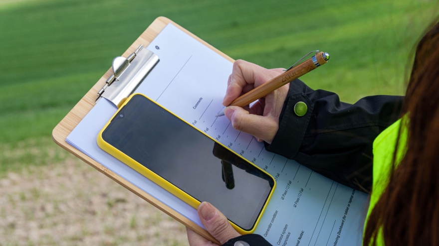 Ingeniero agrónomo tomando notas en un portapapeles y usando el teléfono móvil en un campo de trigo.