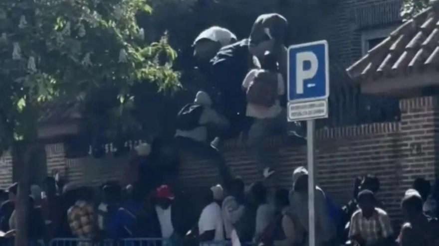 Migrantes intentando saltar la valla de la embajada de Gambia en Madrid tras varias horas de espera para conseguir la regularización