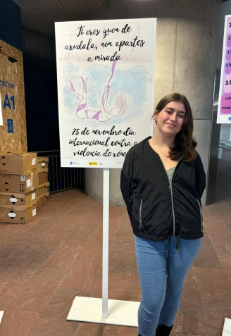 Ainhoa Díaz Pérez posa junto al cartel ganador expuesto en el IES MIlladoiro