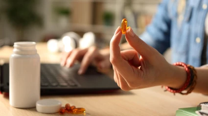 Primer plano de la mano de una estudiante que muestra un estudio que muestra una pastilla de vitaminas por la noche sentada en un escritorio en casa