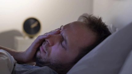 Concepto de insomnio y pesadillas. Un hombre no puede dormir después de una fiesta, se acuesta en la cama por la noche y tiene el despertador sobre la mesilla de noche. Trastornos del ciclo sueño/vigilia