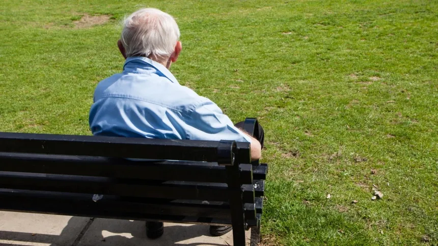 Un hombre anciano en un banco mirando hacia el parque