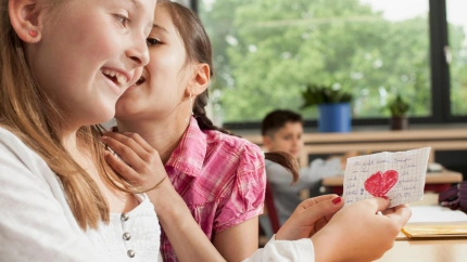 Dos niñas susurran en clase mientras una de ellas sujeta una carta de amor