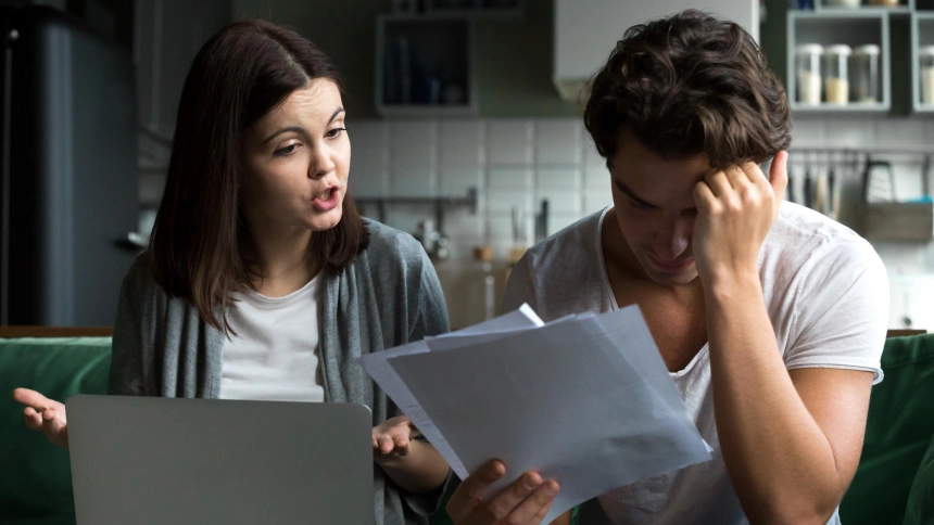 Angry wife scolding blaming upset husband of unpaid bills, bankruptcy or past due debt, unhappy millennial couple having financial problems arguing at home sitting on sofa with laptop and papers
