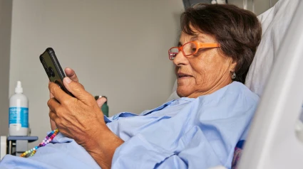 Una señora tumbada en una camilla de hospital mira su teléfono móvil