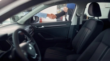 Apretón de manos para acordar la compra de un vehículo visto a través de la ventanilla del coche