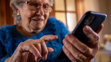 Una mujer de avanzada edad utiliza un teléfono móvil mientras sonríe