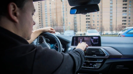 Un hombre conduce un coche moderno mientras toca la pantalla táctil del salpicadero