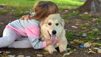 Una niña posando de espaldas mientras abraza a su perro en el parque