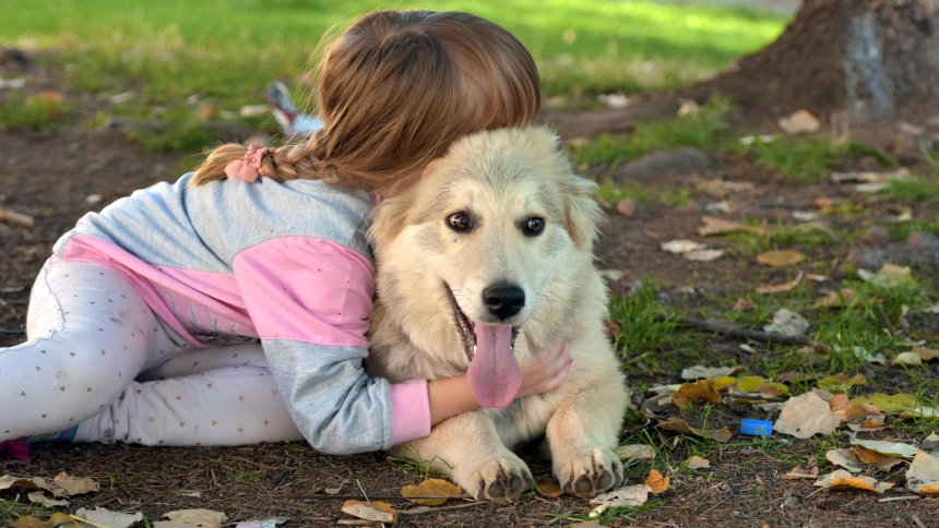 Una niña posando de espaldas mientras abraza a su perro en el parque