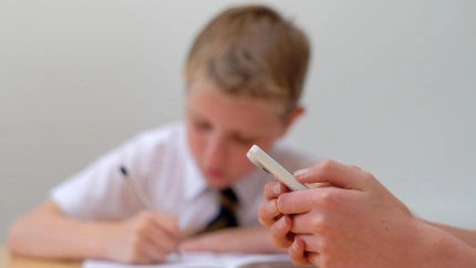 Un alumno utilizando su teléfono móvil en clase mientras un compañero trabaja sin distraerse