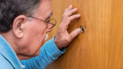 Un señor mayor mirando por la mirilla de su puerta