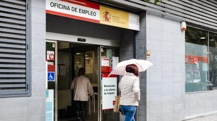 Una mujer con paraguas pasa por la oficina del paro